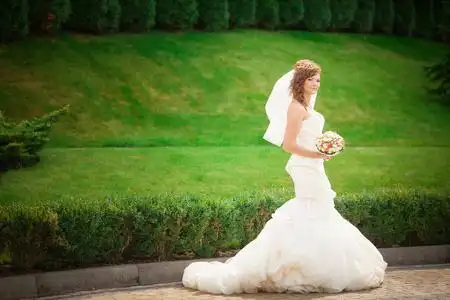 一个美丽年轻性感黑发的新娘,在长长的白色结婚礼服和婚纱站在森林抱