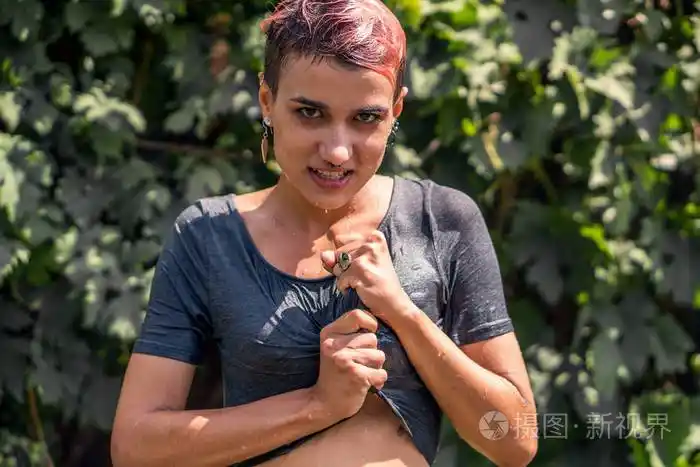 年轻漂亮的穿湿衬衫的女孩, 淋浴后, 从软管在花园.