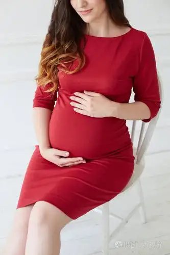 照片 穿红色裙子的孕妇坐在椅子上摸着她的肚子. 怀孕概念期待女性.
