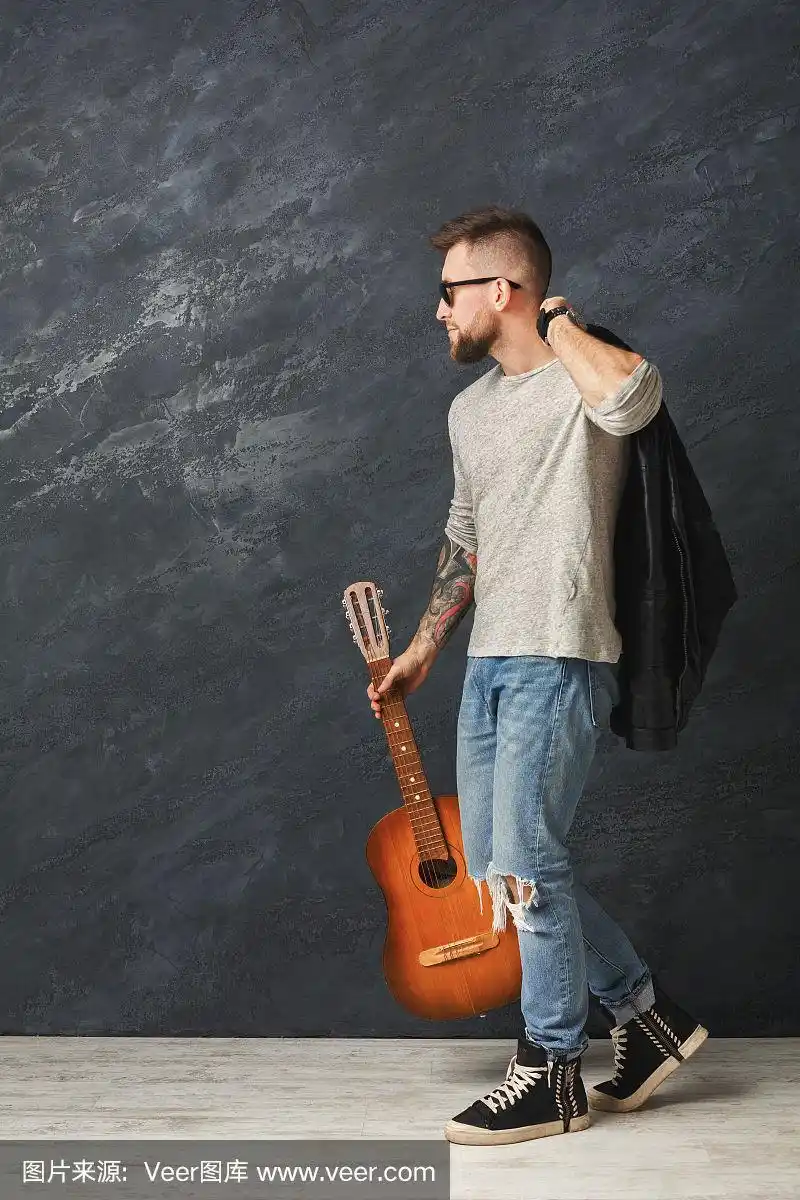 英俊的微笑男子与吉他摆姿势在工作室