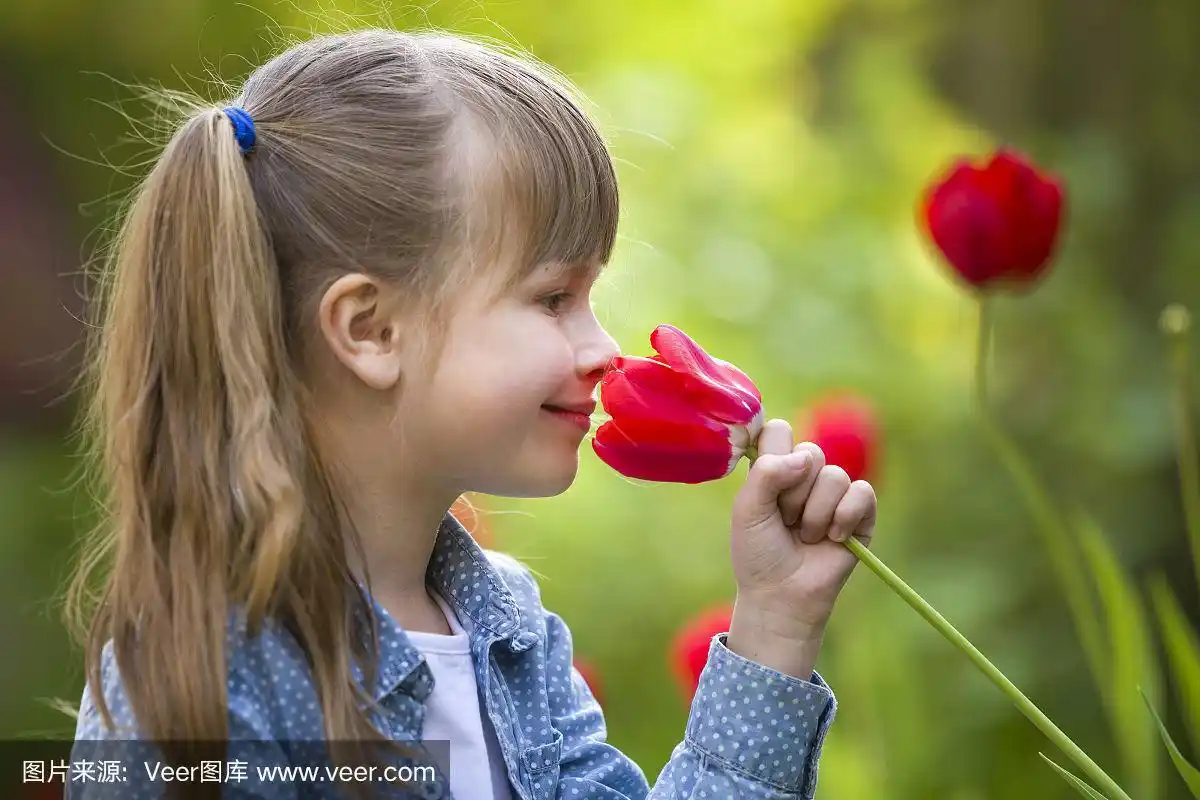 可爱的漂亮微笑的小女孩的侧面与灰色的眼睛和长头发闻明亮的红色