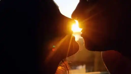 初吻浪漫的年轻情侣剪影亲吻日落与太阳在地平线上闪耀在他们后面.