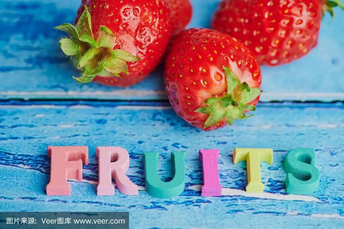 英文单词fruit在蓝色背景下的草莓前面用木制的彩色字母排列