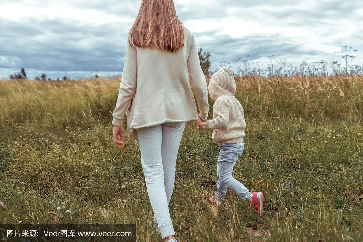 妈妈女人在秋天的公园里牵着孩子的手,小男孩3-5岁的儿子,在大自然中