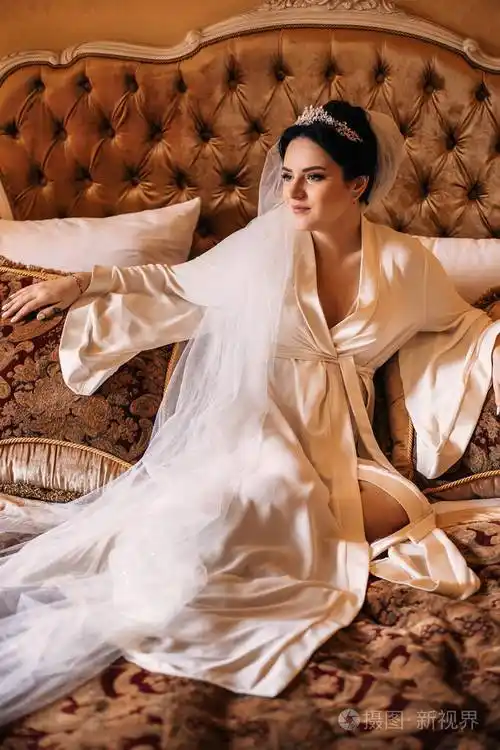 新娘坐在枕头中间的床上穿着浴袍和婚礼的新娘