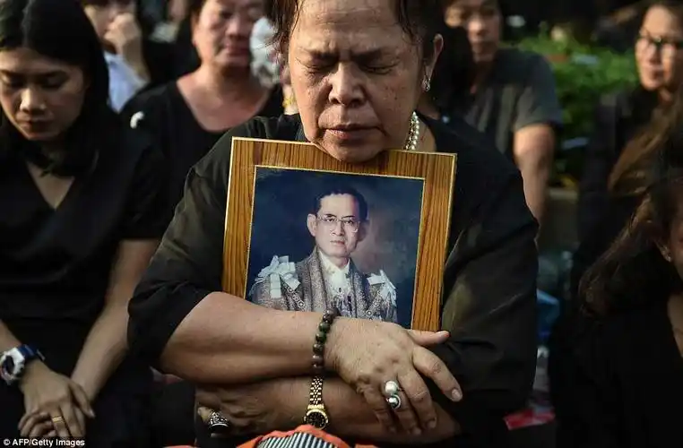 泰国曼谷,一名悼念者怀抱泰国国王密蓬·阿杜德的照片,载着他遗体的