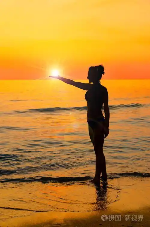 坚强自信的女人在海边日出的阳光下张开手臂