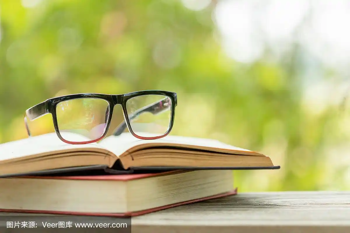 书和眼镜放在抽象的绿色自然模糊背景的木桌上.阅读与教育理念
