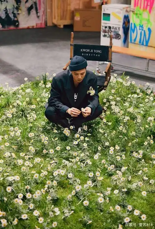 在视频中,权志龙一身黑色西装,坐在他最爱的雏菊花中,毛线帽,金丝边