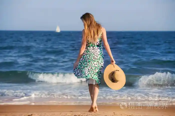 年轻女子赤脚行走在海洋上的帽子沙滩在阳光明媚的天热和享受假期.