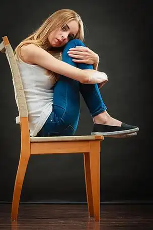 年轻悲伤孤独的女人蜷缩在椅子上