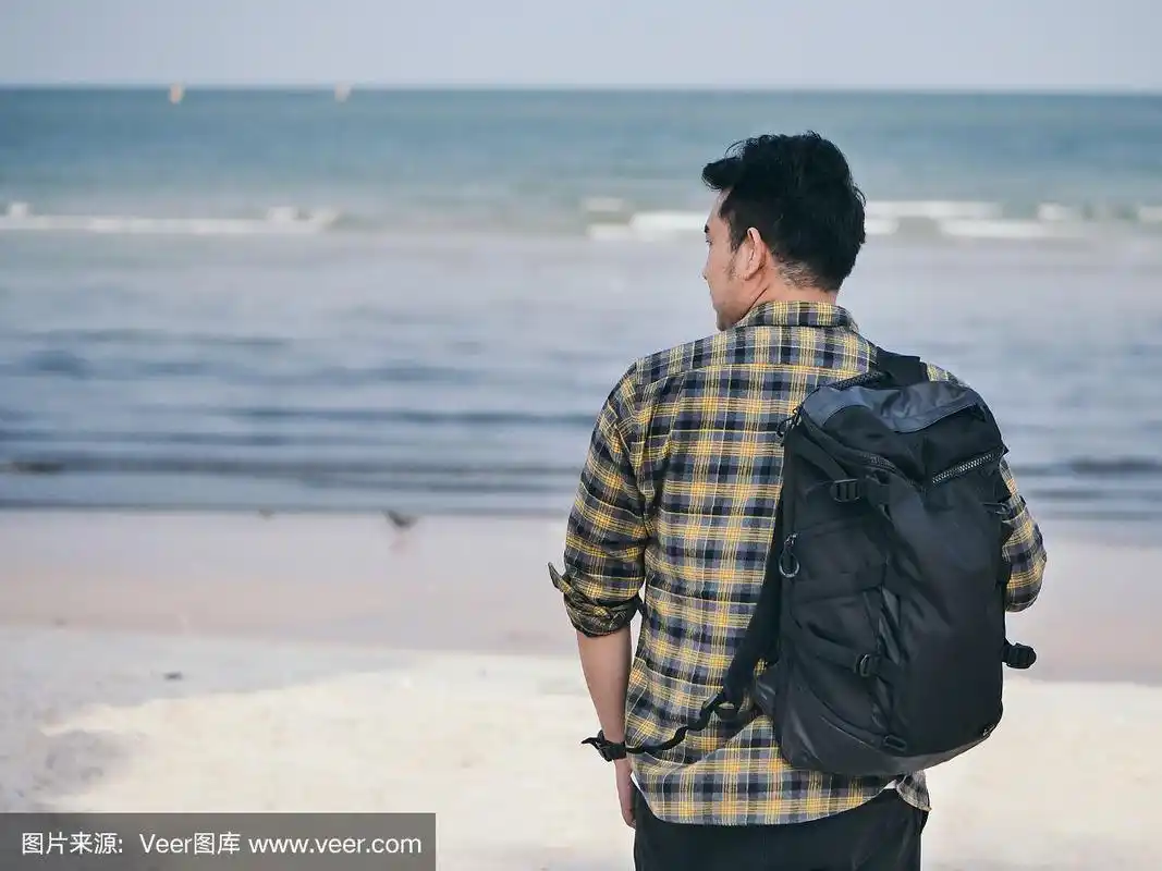 一个背着背包的亚洲男人站在沙滩上.