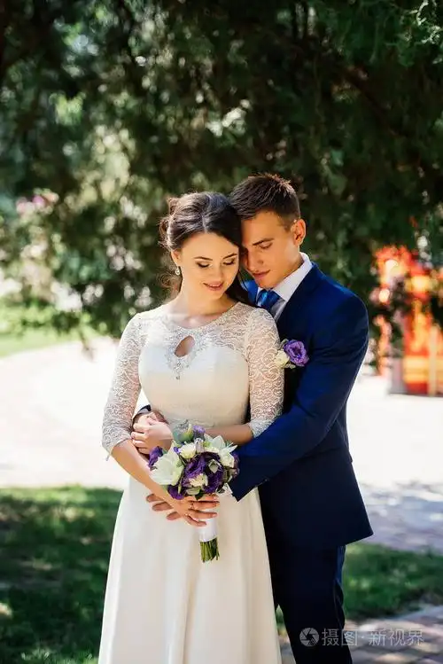新娘和新郎拥抱在公园里新郎抱新娘新婚夫妇在婚礼那天的爱