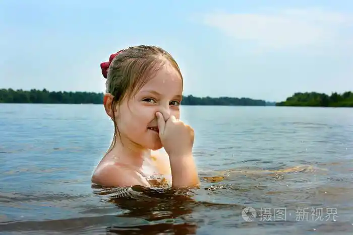 一个湿头可爱的小女孩在河里游泳她用手pinchs她的鼻子