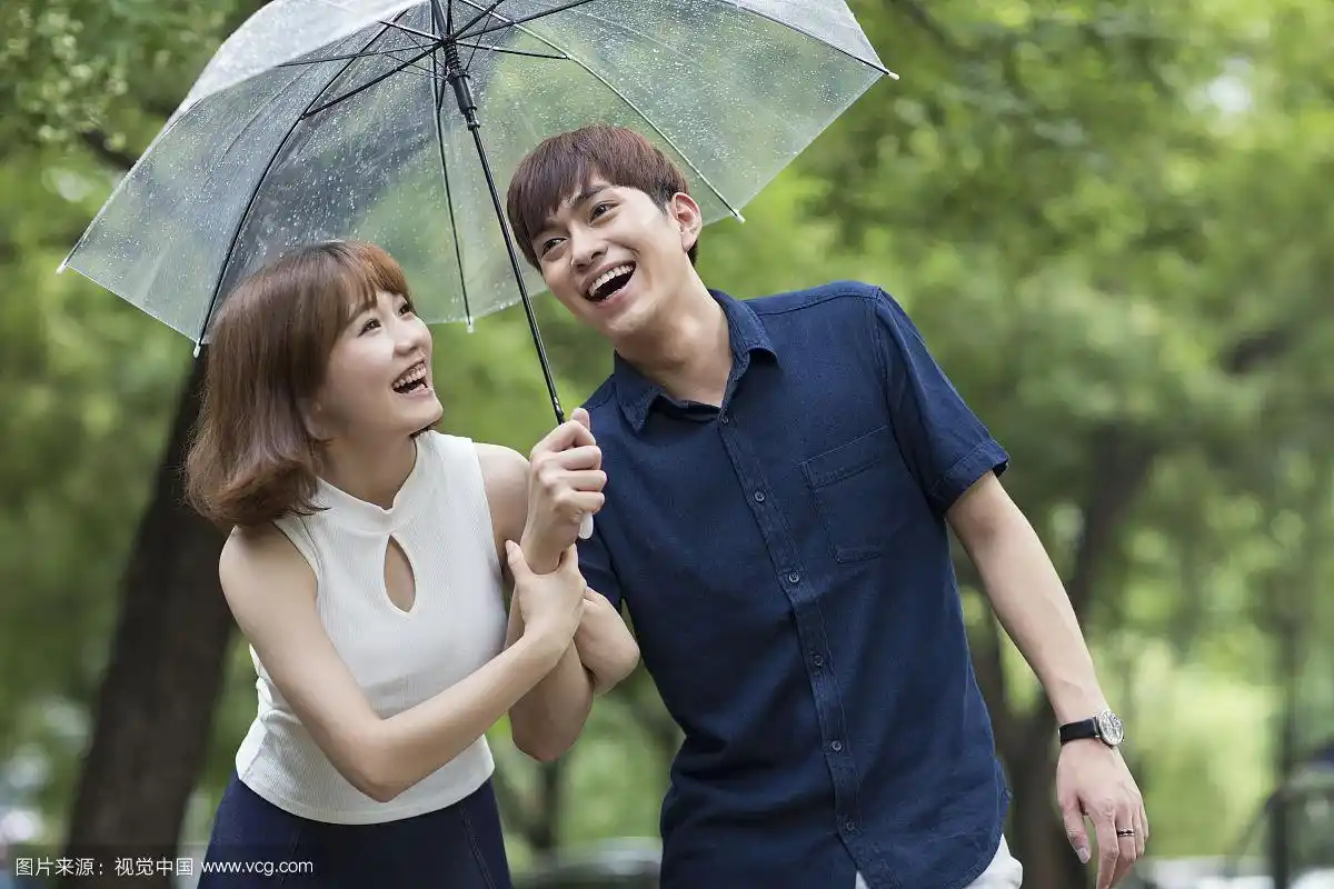 快乐的年轻情侣打着雨伞散步