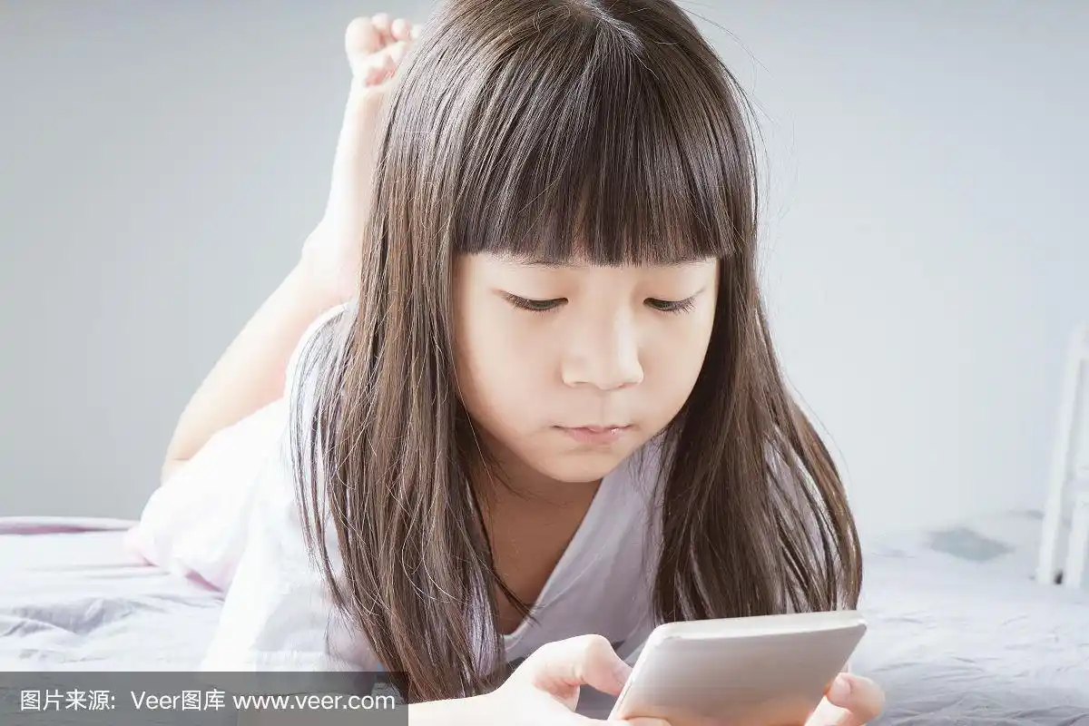 一个亚洲小女孩躺在床上玩智能手机.孩子沉迷于手机.