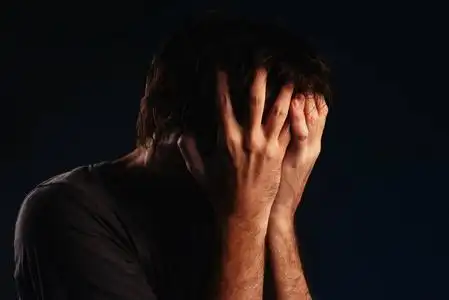 男人绝望地哭泣,双手捂脸,低键肖像照片