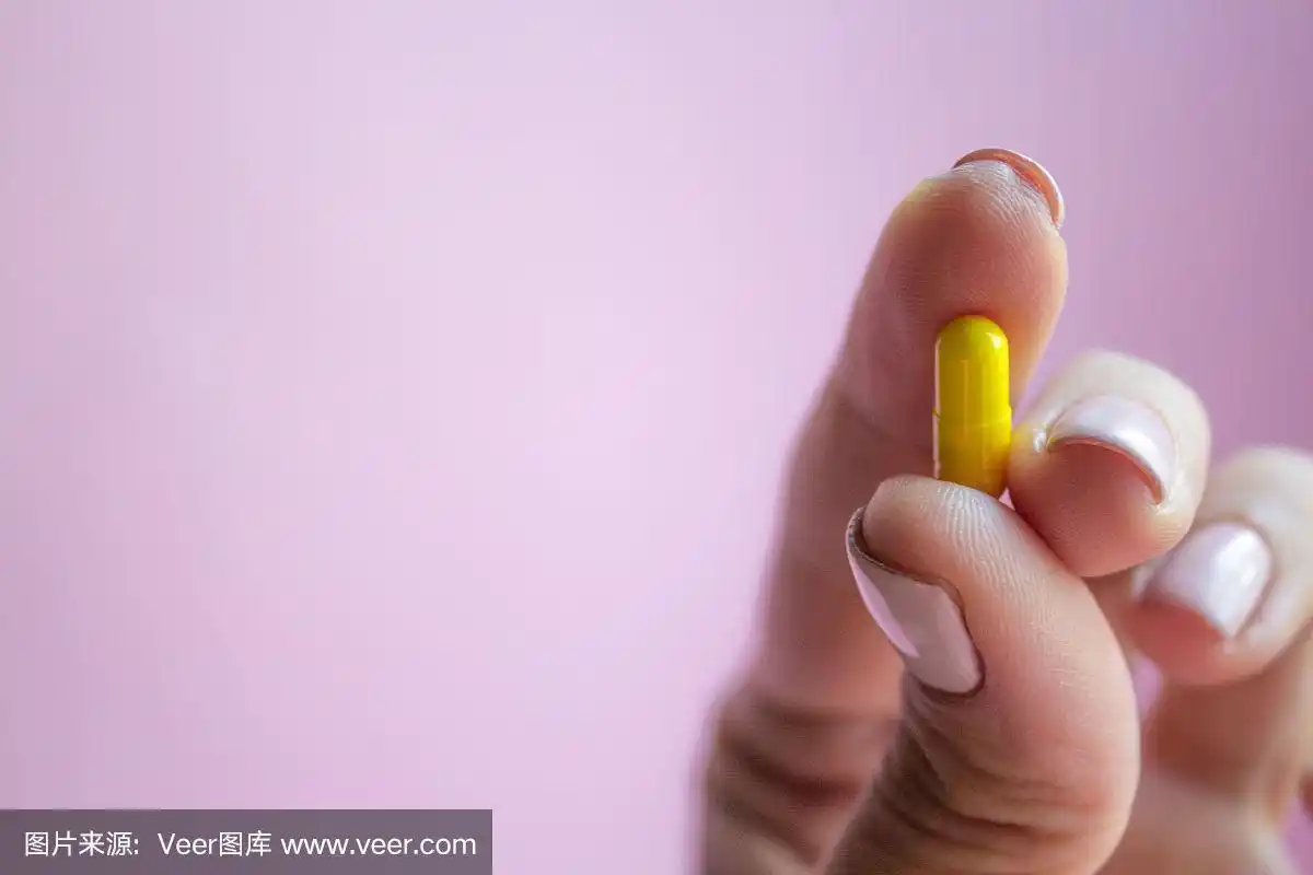 女人手拿黄色药丸胶囊在粉红色的背景,药物概念与拷贝空间
