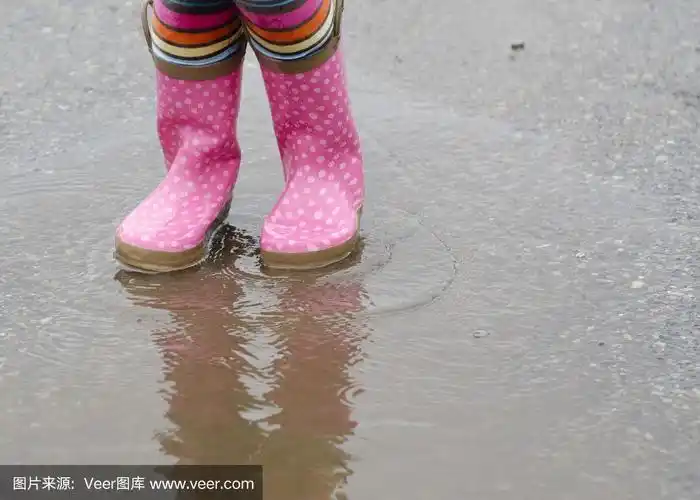 小女孩穿着雨靴在水坑里戏水