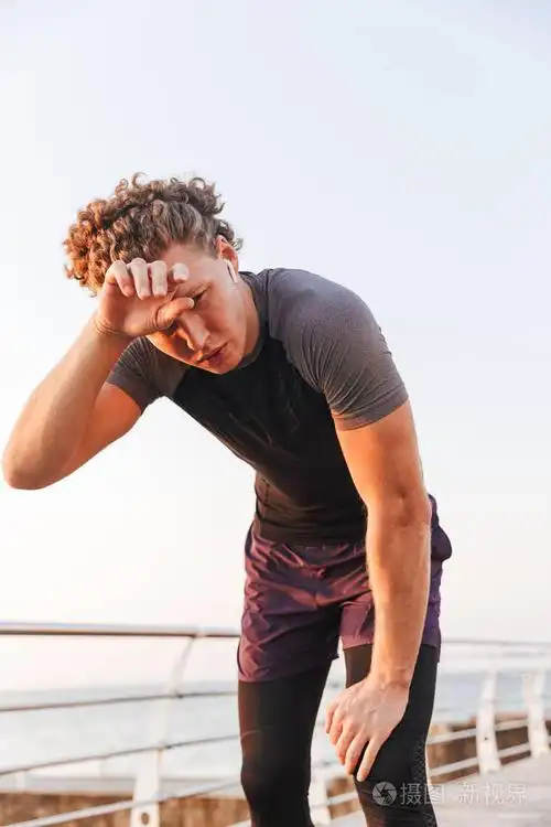 在海滩锻炼后休息的出汗运动员的肖像, 听音乐与耳机照片-正版商用