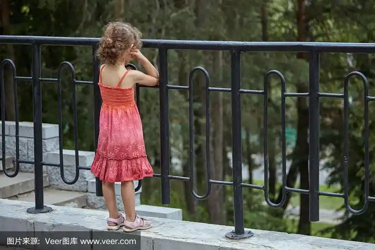 一个孤独的小女孩透过金属栅栏望出去的背影