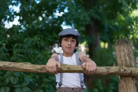 一个穿着带吊带裤和一件无袖衬衫的男孩在木栅栏附近的肖像.照片