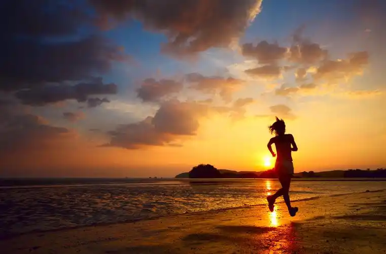 年轻女子在日落时在海岸跑步