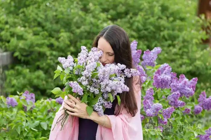 美丽的年轻女孩与一束丁香花在花园里