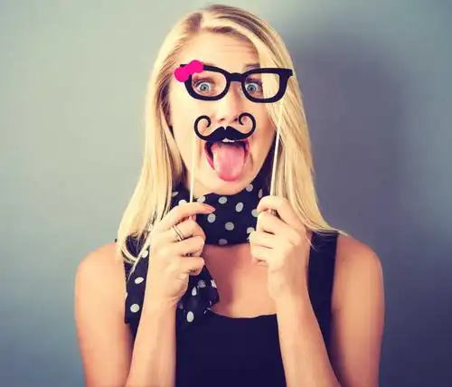 粉红色背景下拿着眼镜框和胡子框搞怪拍照的美女