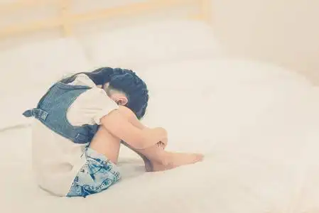 坐在床上,她抱着膝盖在难过的时候喜怒无常的郁闷亚洲小女孩照片