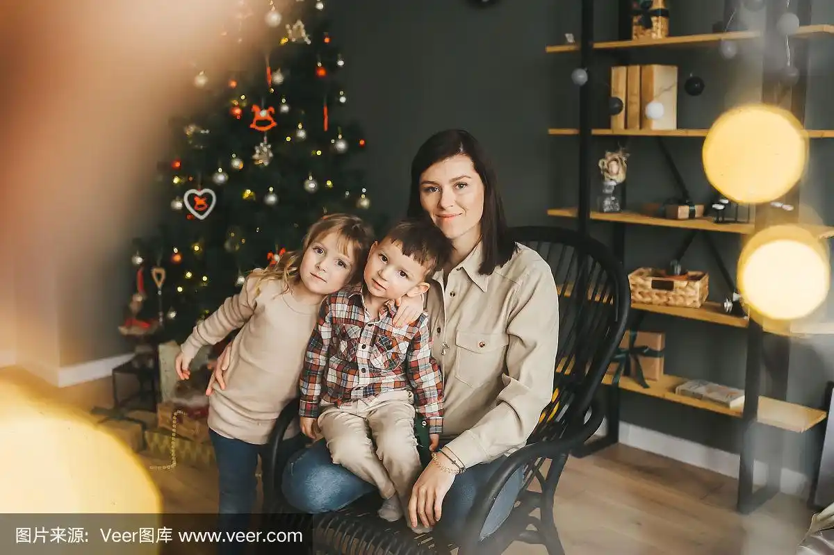 快乐的母亲和两个孩子的肖像靠近圣诞树.背景是一棵圣诞树.