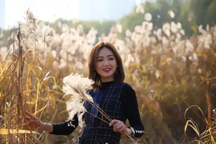 右手抬起轻抚,左手持花,眼神远视.虚化前后景芦花,突出人物动作表情.