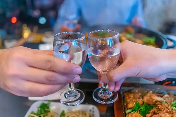 中国餐饮行业,饭店的餐桌上两只端着白酒的手在碰杯图片下载