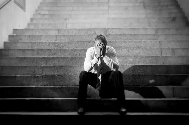 坐在阴暗楼梯上捂着脸哭泣的悲伤的中年男性孤独的男人失败难过疲劳