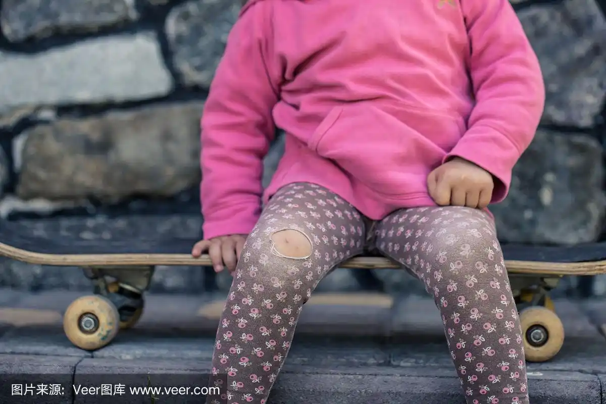一个漂亮的小女孩在滑板上摔倒了,膝盖擦伤了,特写镜头是她的手.
