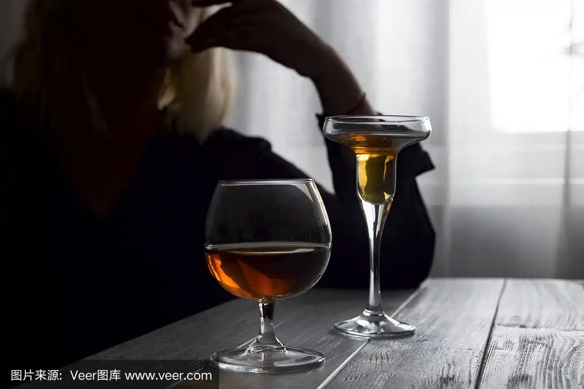 年轻美丽的女人抑郁,在黑暗的背景下喝酒