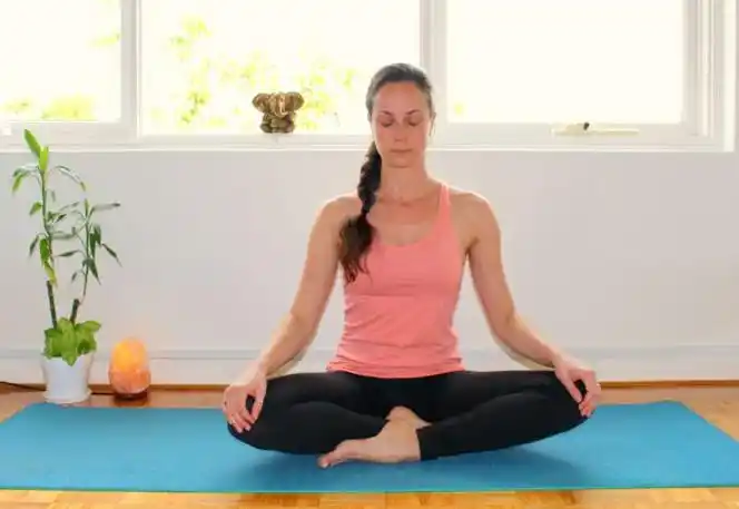 坐在瑜伽垫上,双腿盘坐着,上半身挺直,双手自然搭在双腿膝盖处.