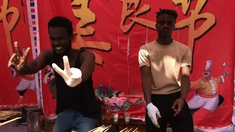 非洲黑人小伙边舞边卖羊肉串,暗背景下白手套特别显眼眼