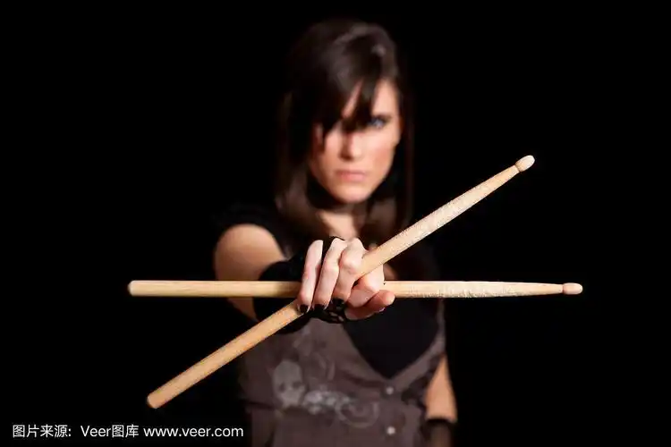 强硬的摇滚女孩拿着鼓棒在黑色的背景