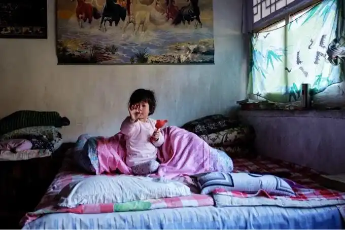 赖在炕上玩耍的山村小女孩