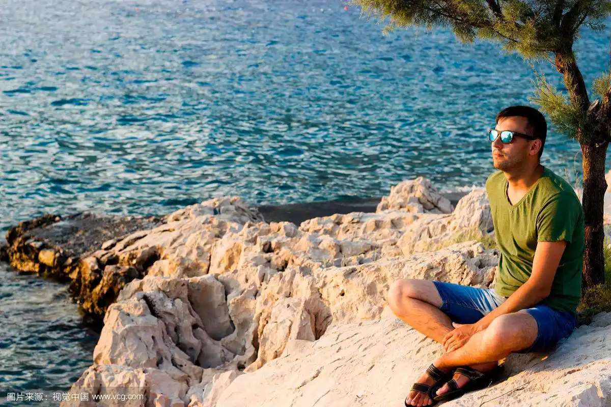 戴着墨镜坐在海边的男人