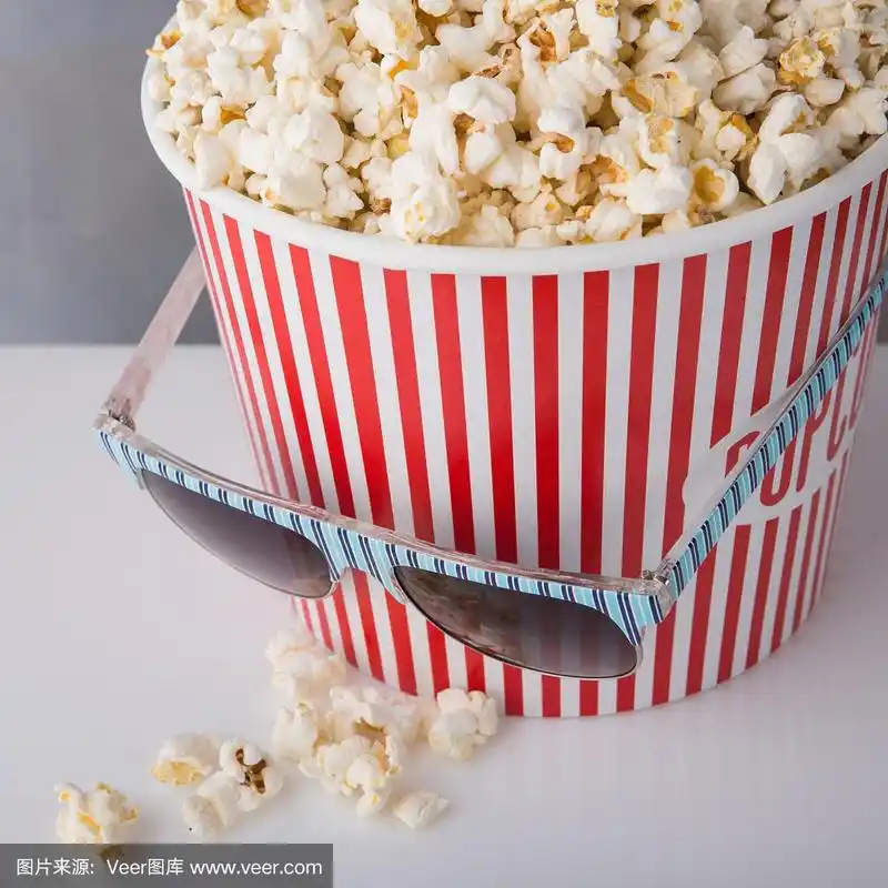 生病的纸板箱里装着一条红色长条的爆米花,在容器上放着玻璃杯,爆米花