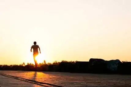 年轻男子赛跑者的剪影在公园里奔跑在黄昏日落.人们走路和运动.