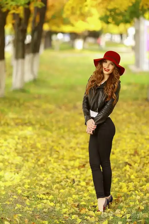 美丽优雅的女人站在时尚的红色帽子在一个公园在秋天里