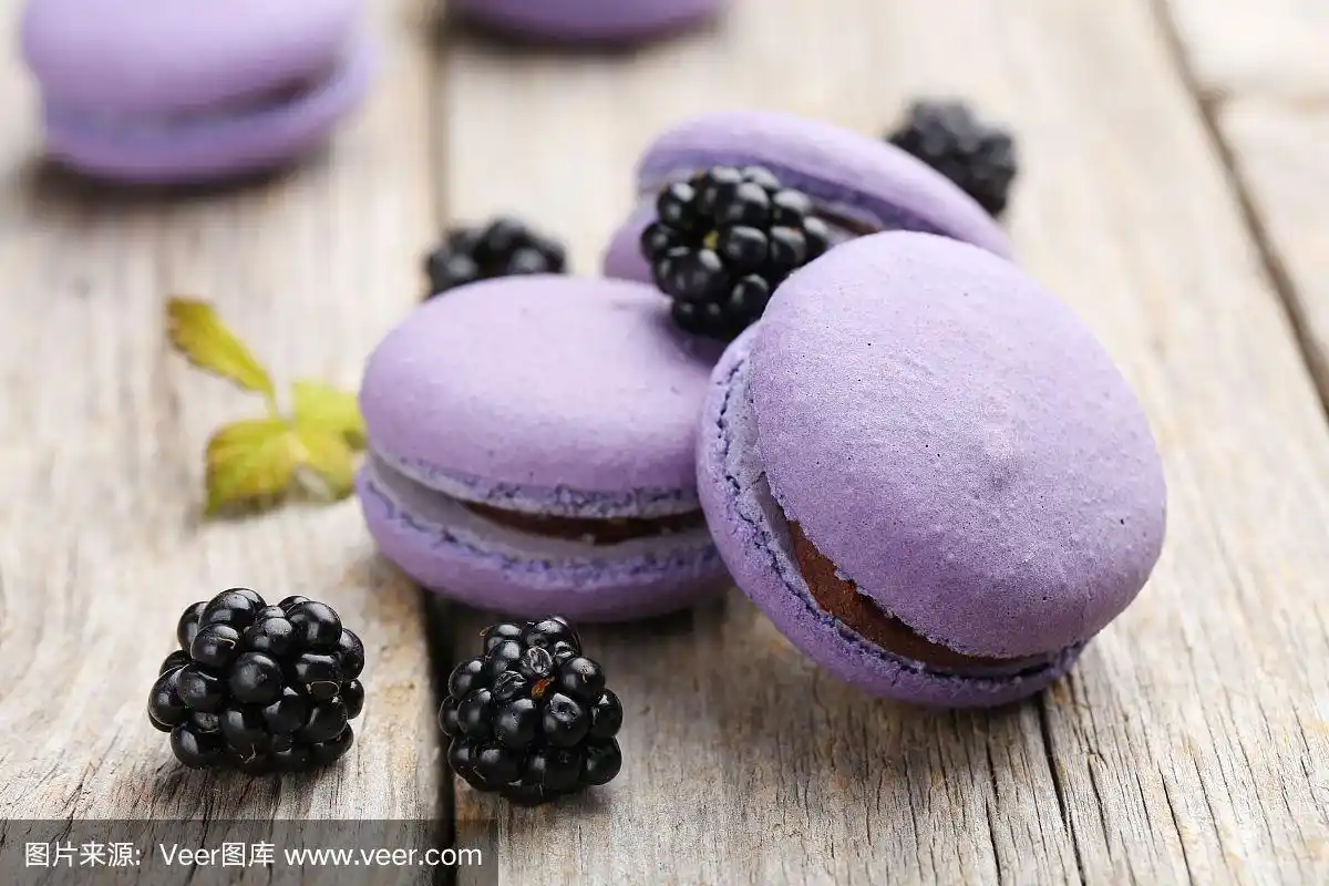 美味的紫色马卡龙与黑莓在灰色的木制背景