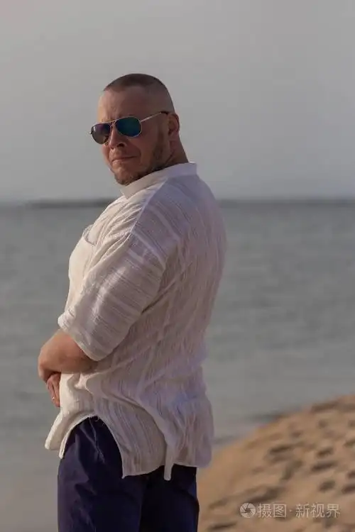 一个穿着白衬衫戴着太阳镜的男人在海边的沙滩上摆姿势