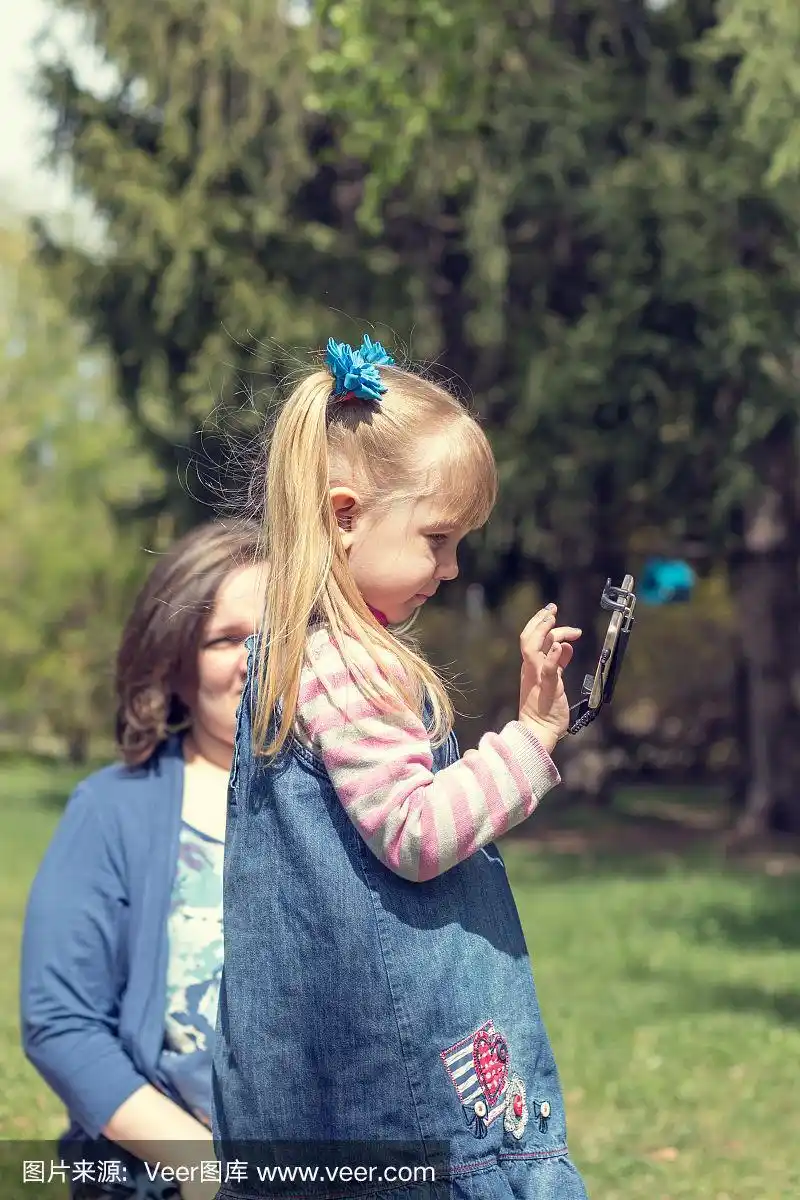 可爱的金发小女孩梳着两个马尾辫在春天的阳光明媚的一天在城市公园里