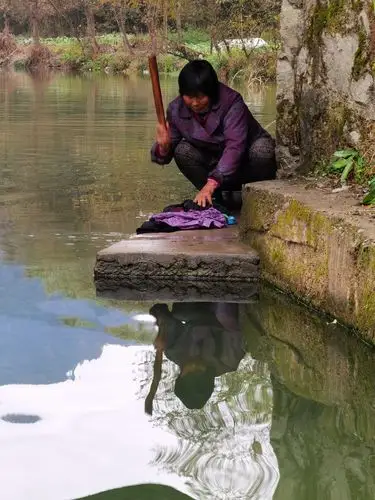 在清冽的河边,用棒槌洗衣服的村妇.