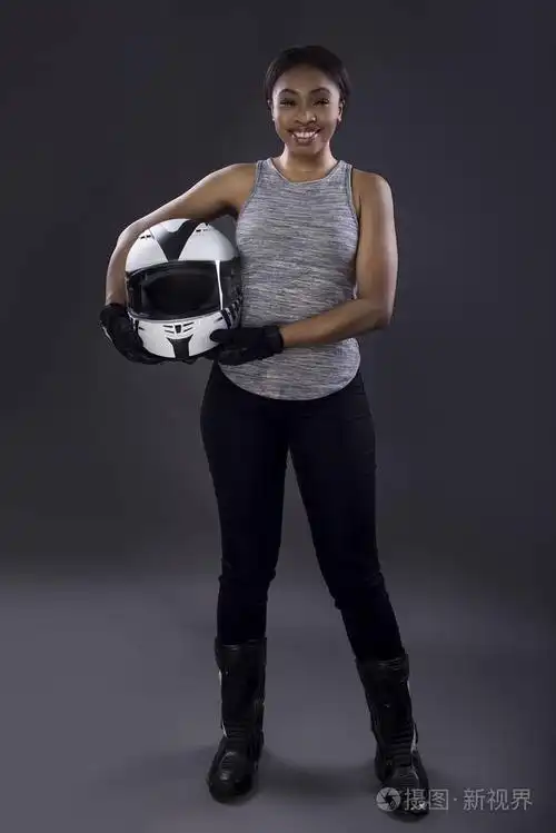 在手持赛车头盔时身穿无袖背心的黑女赛车手或骑自行车的司机或替身该