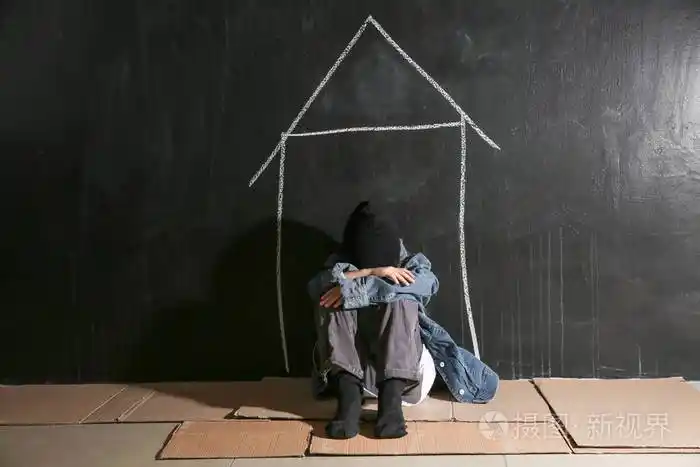 无家可归的小女孩坐在黑暗的墙边的地板上